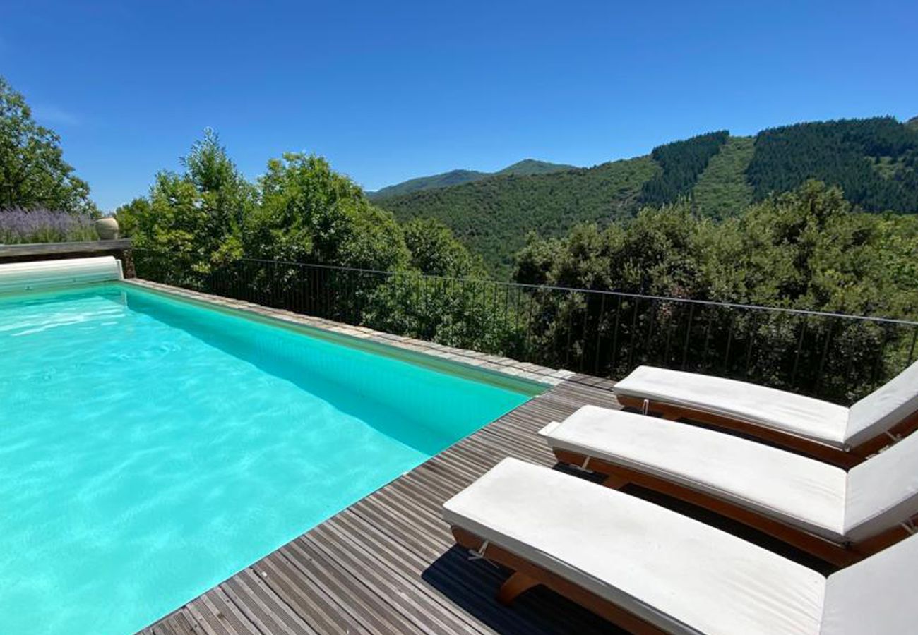 Luxuriösen beheizten Pool bei La Bastide 48BAST, geschmückt mit Sonnenliegen und Sonnenschirmen auf einer Holzterrass