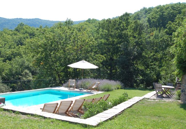 Découvrez la luxueuse piscine chauffée de La Bastide 48BAST, ornée de transats et de parasols sur une terrasse en bois